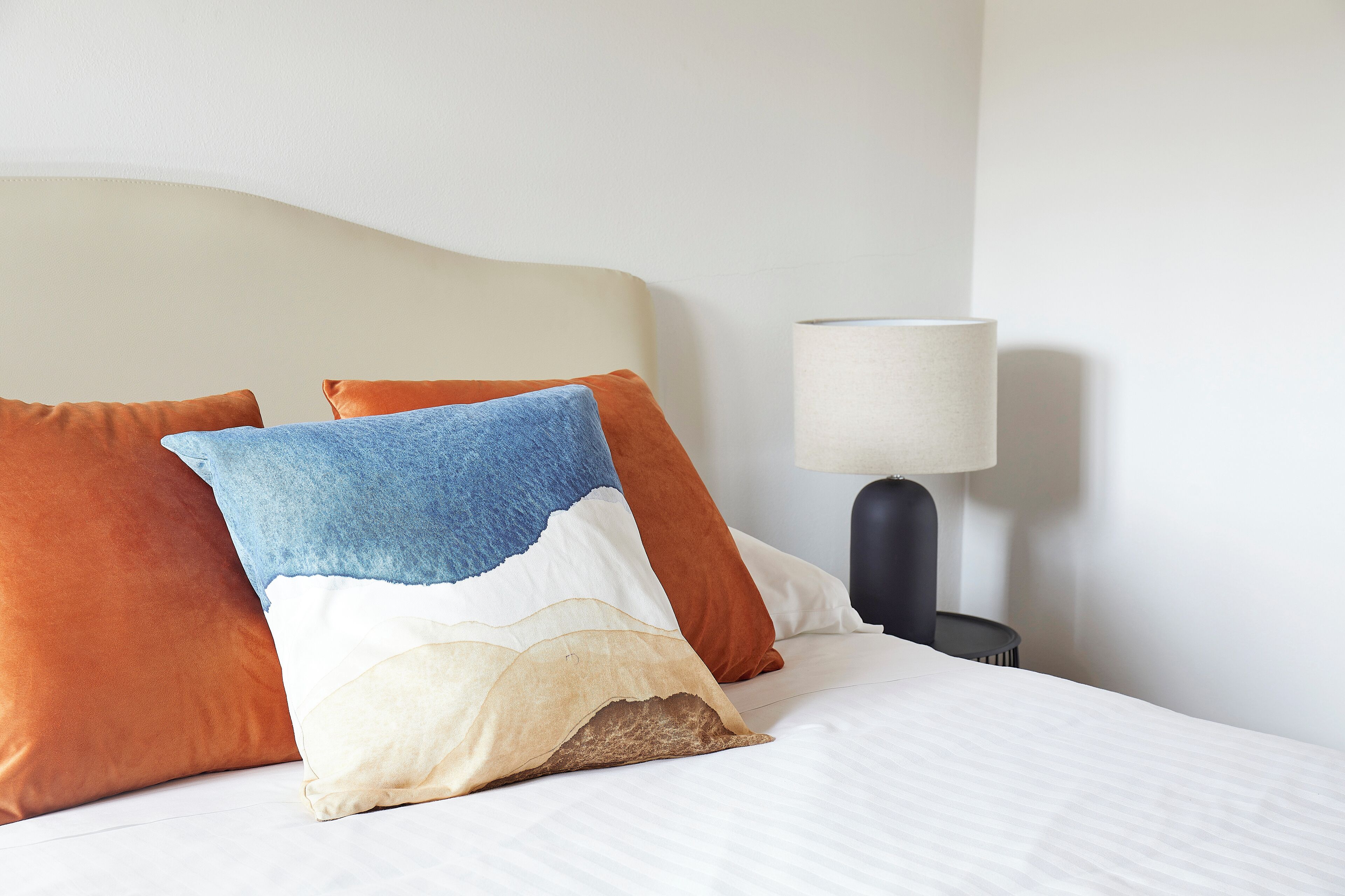 Un lit bien fait, avec un drap blanc et trois oreillers de différentes couleurs.