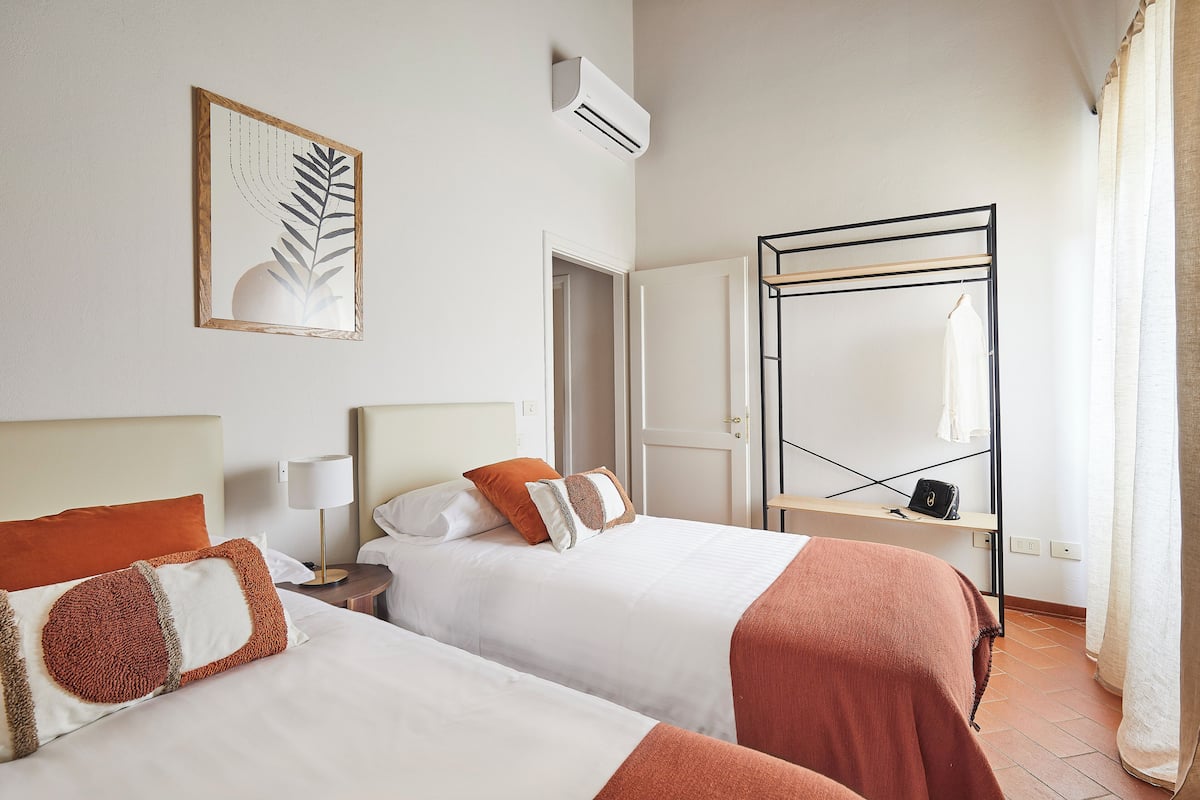 A hotel room with two beds, a wardrobe, a mirror, and a wall-mounted air conditioner.