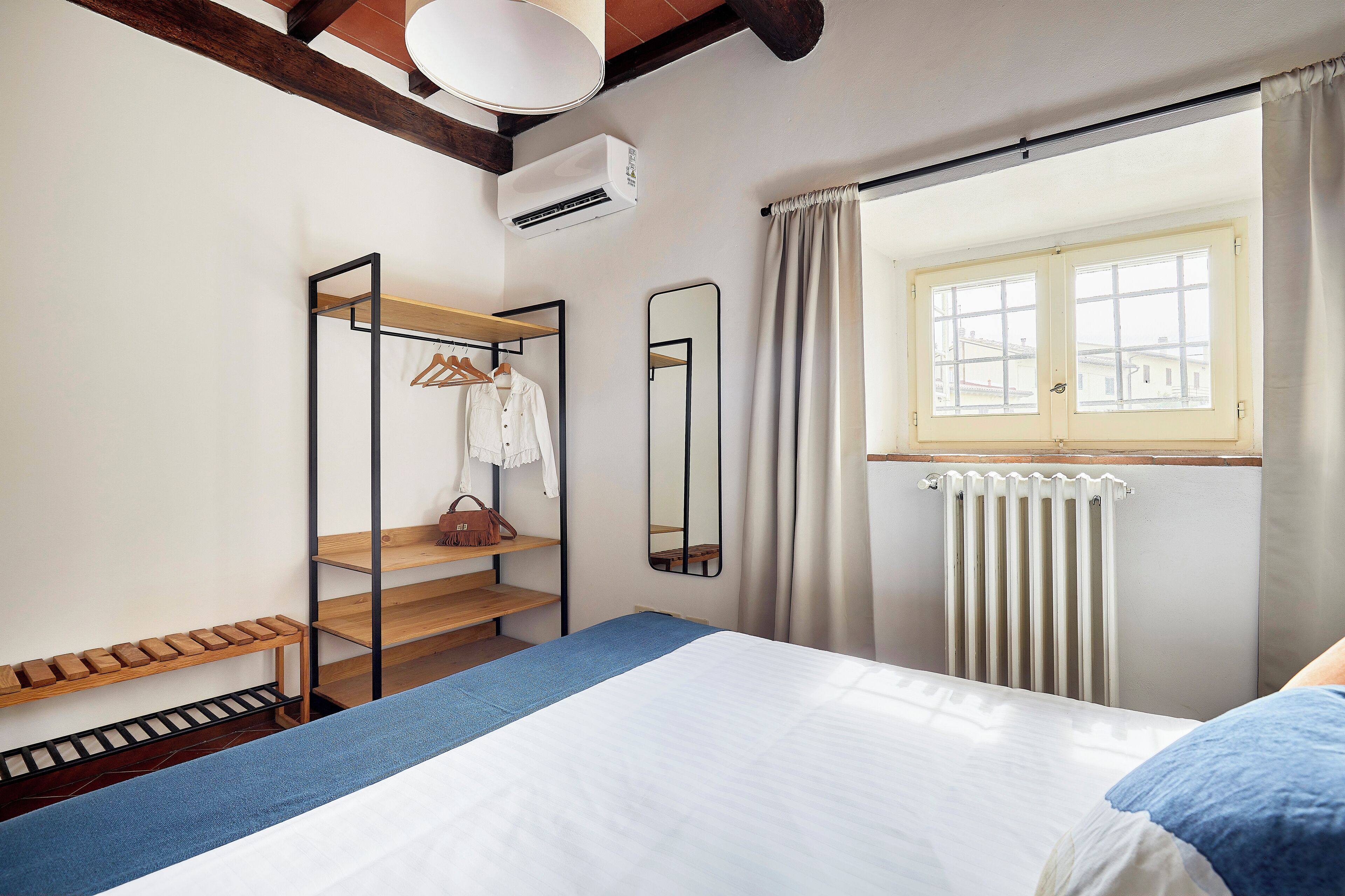 Une chambre à coucher avec un lit, une fenêtre avec des rideaux, un radiateur et un miroir.