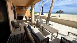 Un patio frente a la playa con mobiliario exterior, una parrilla y vistas al mar.