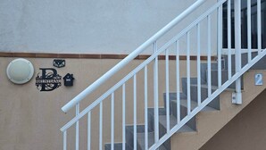 Un escalier avec une rampe blanche mène à un palier. Un luminaire mural et une sonnette sont fixés au-dessus d’une porte.
