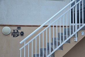 A staircase with a white handrail leading to a landing. There is a wall-mounted light fixture and a doorbell above a door.