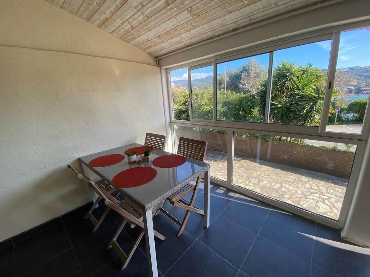 A dining area with a table and chairs, large windows with a view of greenery and hills, and a tiled floor.