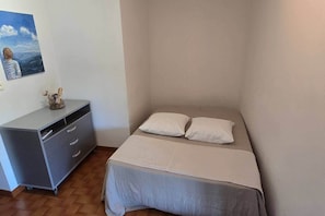 Une petite chambre à coucher, bien rangée, avec un lit simple, une commode et un tableau accroché au mur.