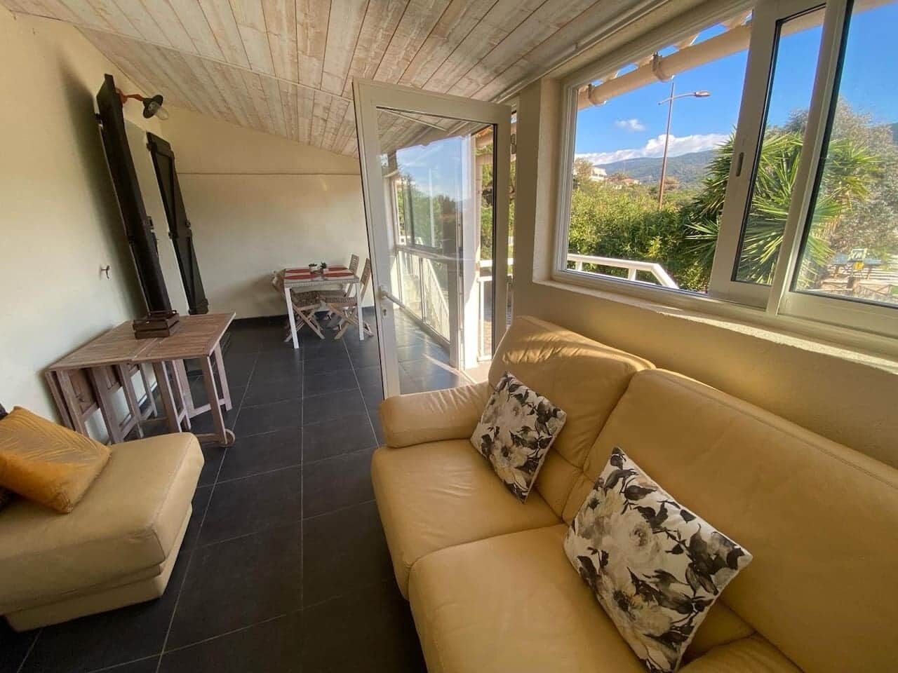 A sunlit room with a beige sofa, a small table, and a view of the outdoors.