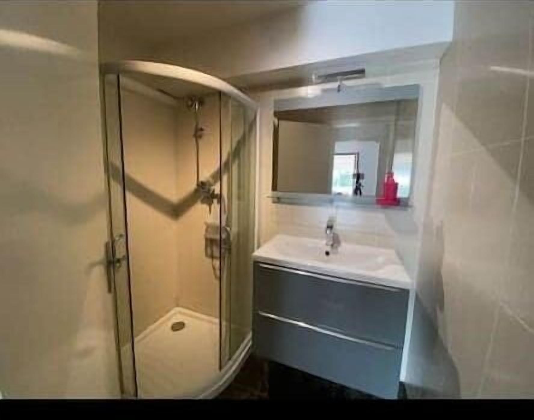 Un baño con ducha de vidrio, lavamanos con espejo y suelo de baldosas.