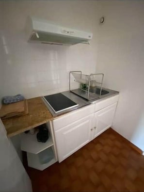 Une cuisine de taille réduite avec des meubles blancs, un plan de travail en bois et une cuisinière intégrée.