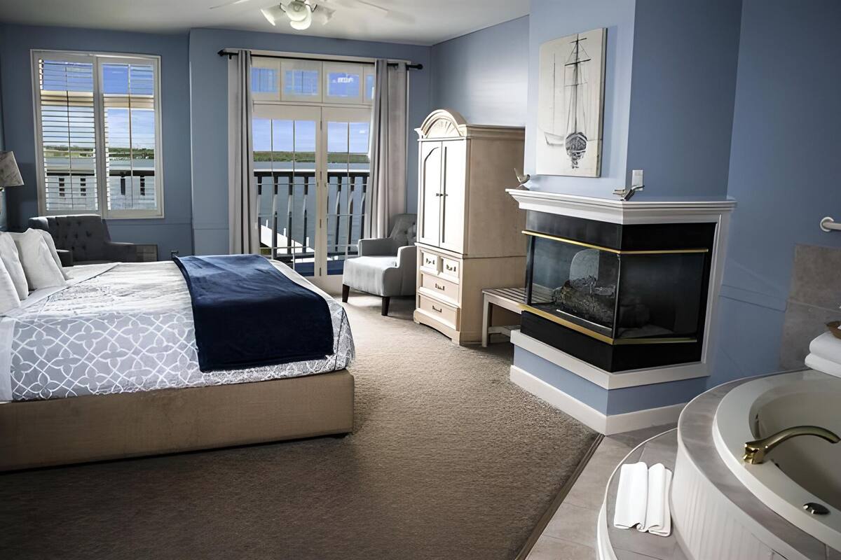 Un dormitorio con cama, escritorio, tocador con bañera y ventana grande con vista al exterior.