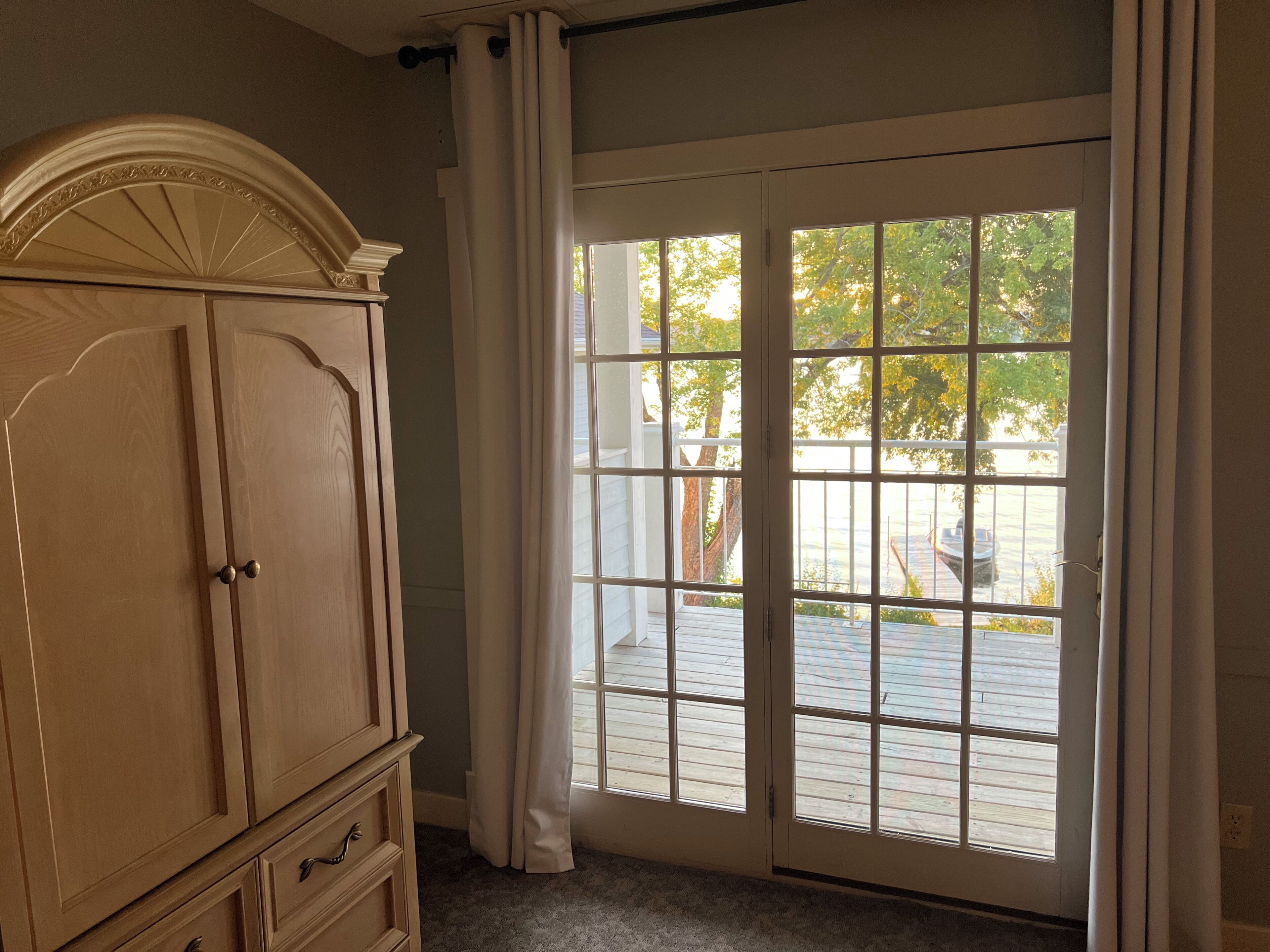 A room with a large wooden wardrobe, a sliding glass door leading to an outdoor deck, and a white curtain.