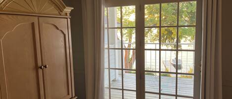 A room with a large wooden wardrobe, a sliding glass door leading to an outdoor deck, and a white curtain.