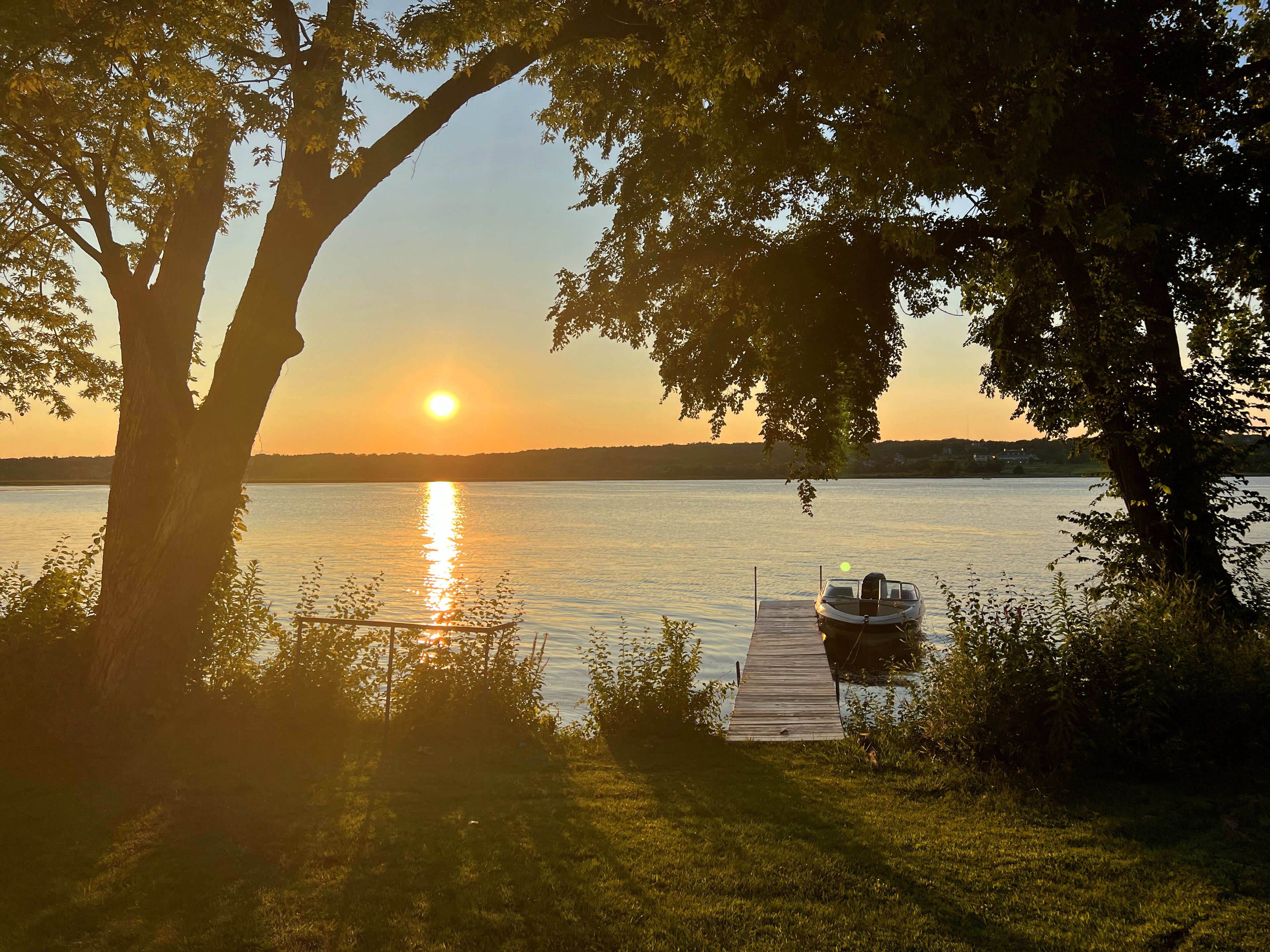 A wooden dock extending into a calm lake at sunset, surrounded by trees.