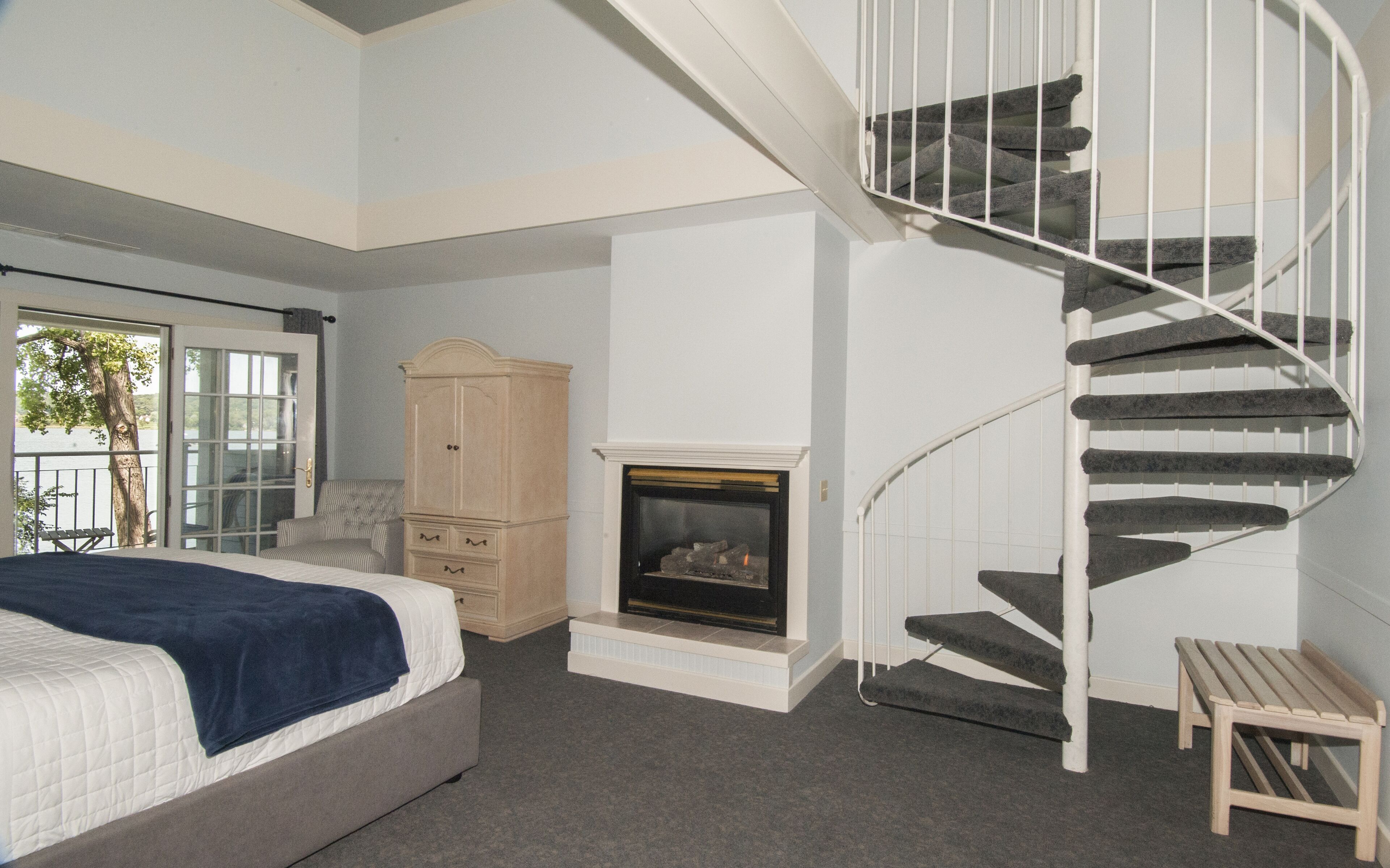 A bedroom with a bed, a wardrobe, a fireplace, and a spiral staircase.