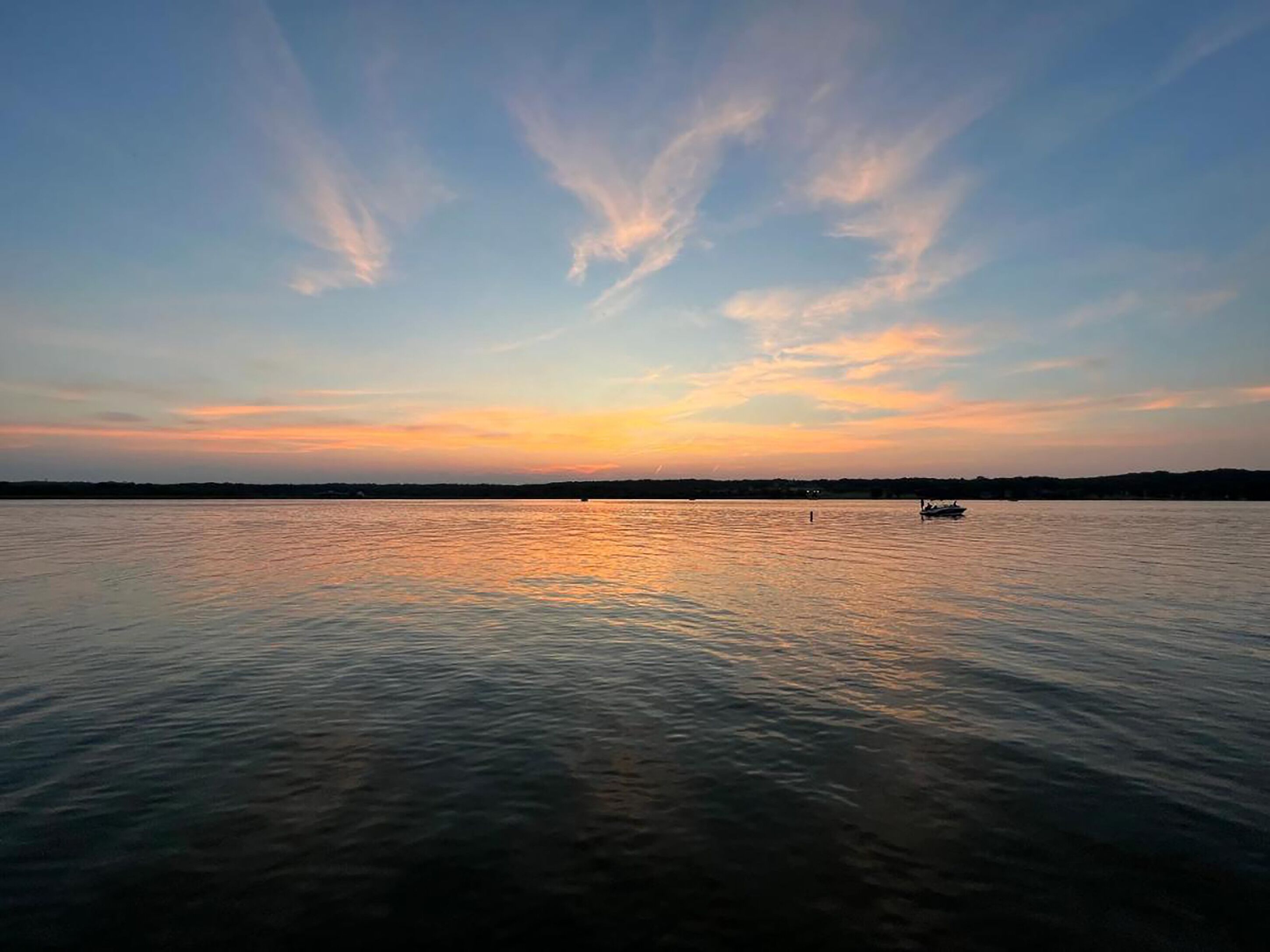 A calm lake at sunset with a boat in the distance.