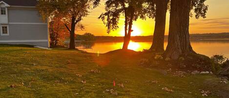 A house with a lawn and trees in front of a body of water during sunset.