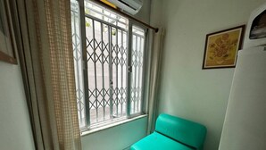 A small room with a teal sofa, a window with metal bars, and a wall-mounted air conditioner. - Studio Sá Ferreira (Copacabana Rio de Janeiro)