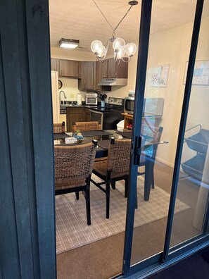 A modern kitchen with dark wooden cabinets, a black countertop, and a dining area with wicker chairs and a glass table.
