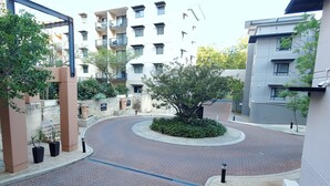 A residential building with multiple balconies, a landscaped courtyard with a central tree, and a brick pathway. - Urban CBD Perth A GEM 1Bedroom Apartment (Perth)