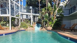 A swimming pool with a waterfall feature, surrounded by lounge chairs and tropical plants. - Coastal Salty Kiss Sleeps 4! (Scarborough)