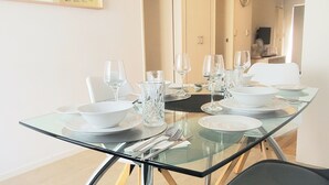 A dining area with a glass table set for six, including wine glasses, plates, and cutlery. - Coastal Salty Kiss Sleeps 4! (Scarborough)