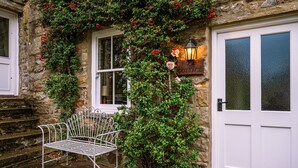A stone cottage with a white door, a bench, and a wall-mounted lantern. - A dales bolthole & quintessential country cottage – cosy, appealing & in an idyllic rural setting (Richmond)