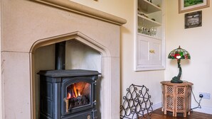 A room with a stone fireplace, a small wooden table with a lamp, and a metal chair. - A dales bolthole & quintessential country cottage – cosy, appealing & in an idyllic rural setting (Richmond)