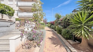 A pathway lined with plants and a building with balconies. - Global Vacacional: Practical flat in Canet Beach (Canet d´en berenguer)