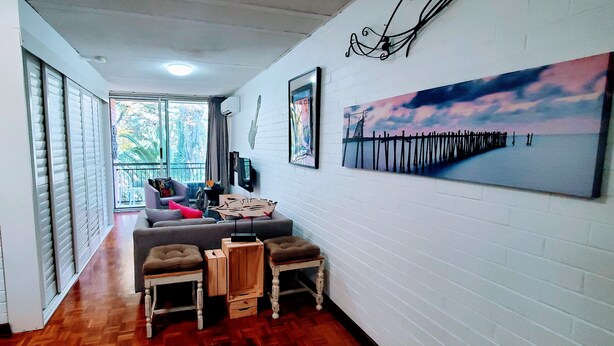 Ein Flur mit einem grauen Sofa, zwei Holzschemeln und einem Gemälde eines Piers.