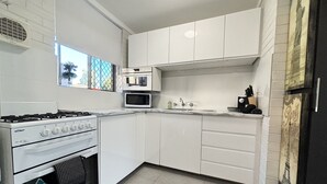 A compact kitchen with white cabinets, a gas stove, a microwave, and a sink. - Serenity & Comfort in Subiaco 1 Bedroom Unit (Subiaco)