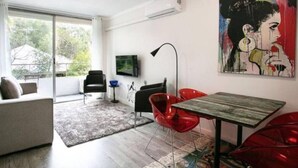 A modern living room with a sofa, red chairs, a dining table, and a large painting on the wall. - Serenity & Comfort in Subiaco 1 Bedroom Unit (Subiaco)