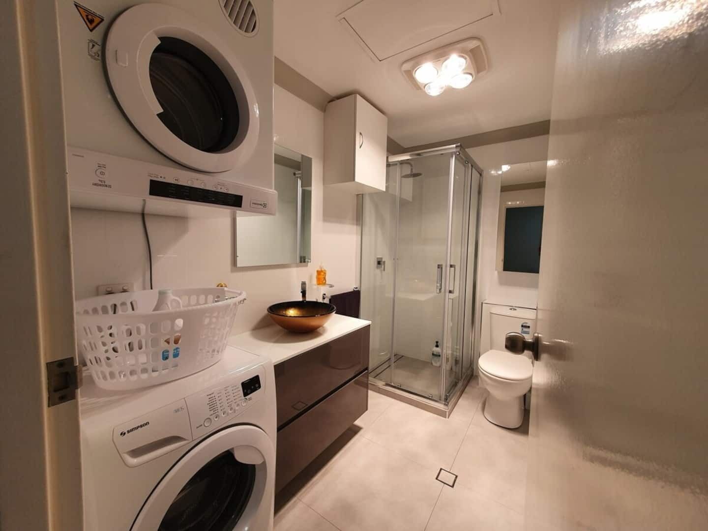 A modern bathroom with a washing machine, a glass shower enclosure, and a toilet.