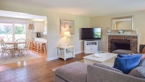 A living room with a fireplace, a television, and a dining area with wooden chairs and a table.
