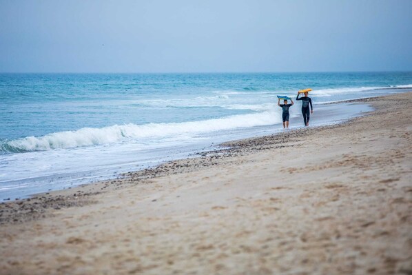 A beach with two people walking, each carrying a surfboard. - Walk to Skaket Beach, Great Backyard! (Orleans)