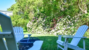 A garden with white Adirondack chairs and a grill.