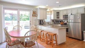 A kitchen with white cabinets, a central island with stools, a refrigerator, and a microwave.