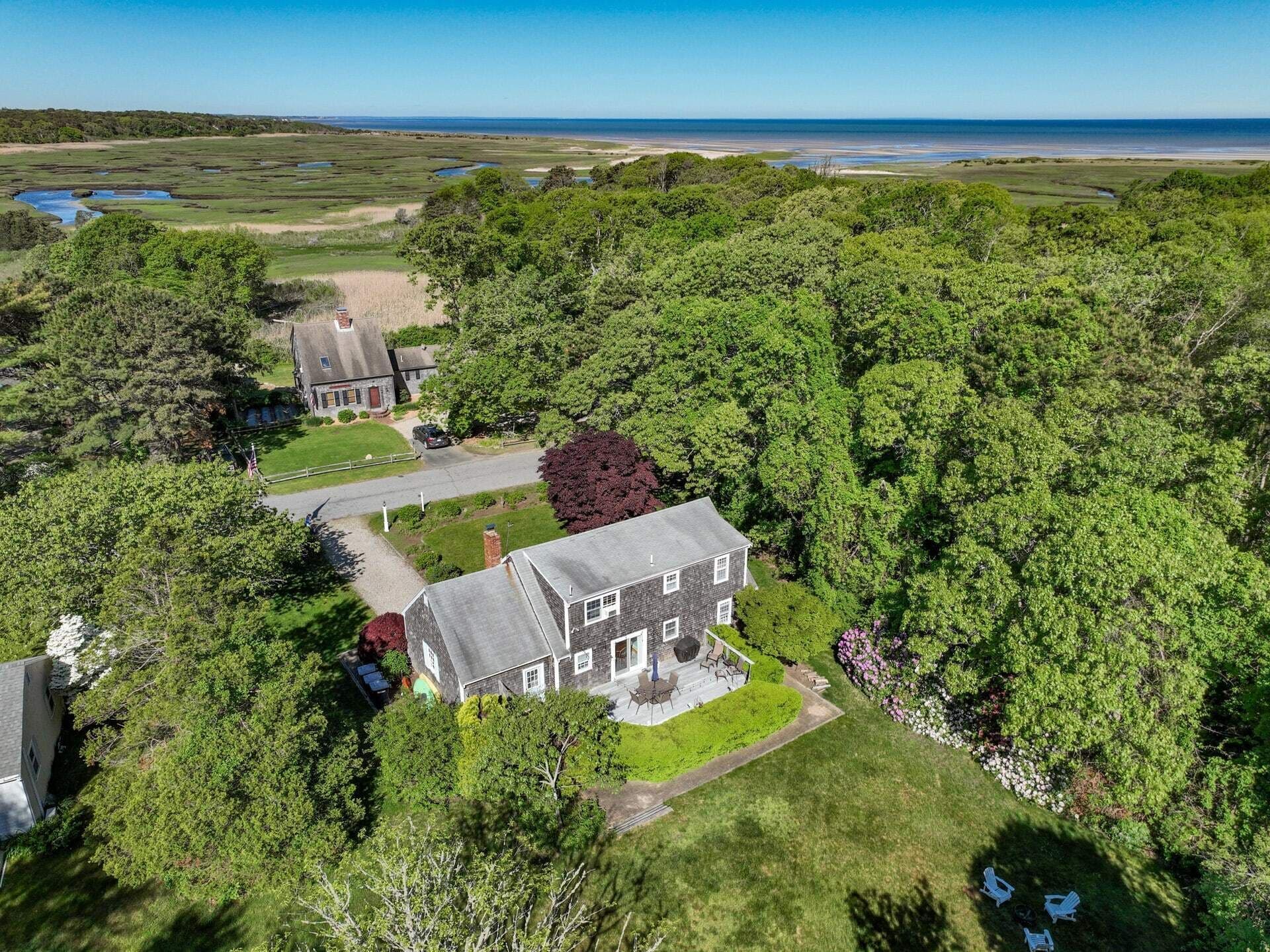 A large house surrounded by dense trees, with a view of the ocean in the background.