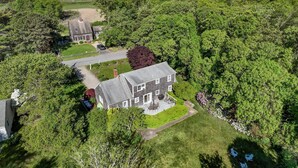A large house surrounded by dense trees, with a view of the ocean in the background.