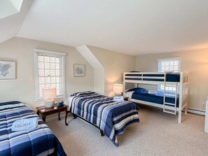 A bedroom with two single beds and a bunk bed, each with 'DELMAR' branded bedding. There are two bedside tables with lamps, a window with blinds, and a framed picture on the wall. - Walk to Skaket Beach, Great Backyard! (Orleans)