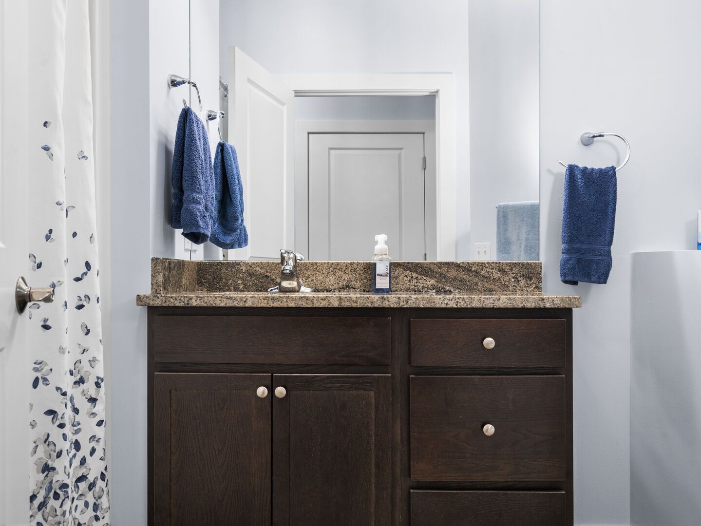 A bathroom with a dark wood vanity, a granite countertop, a mirror, and two towels hanging on towel rings.