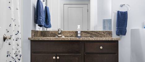 A bathroom with a dark wood vanity, a granite countertop, a mirror, and two towels hanging on towel rings.
