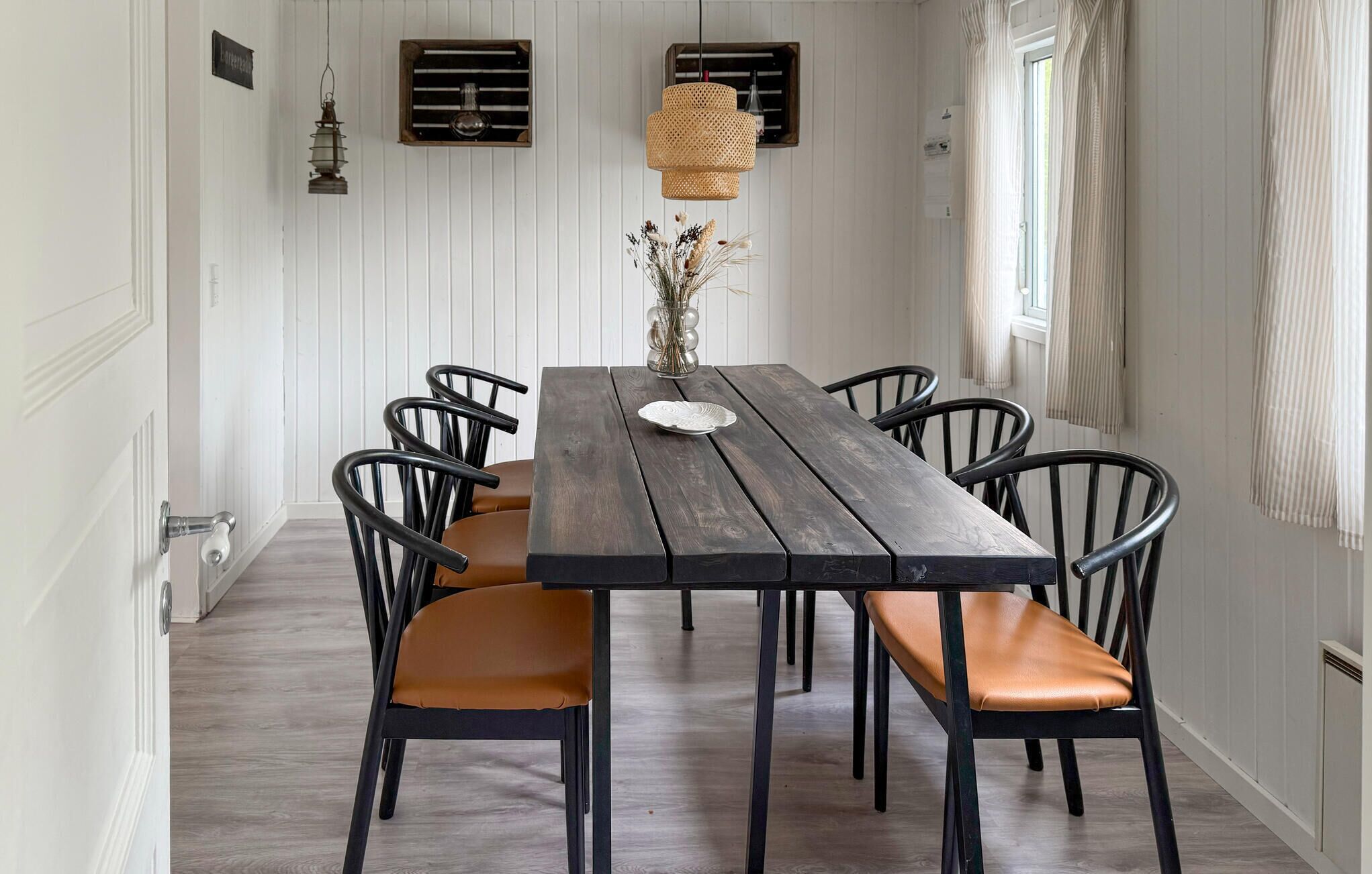 A dining table with six chairs, a vase with dried flowers, and two wall-mounted light fixtures.