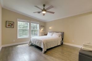 Une chambre à coucher avec un lit, deux fenêtres, un ventilateur de plafond et une table de chevet.