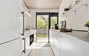 A narrow kitchen with white cabinets, a built-in oven, and a window leading to a garden. - 2 bedroom nice home in Kirke Hyllinge (Kirke Hyllinge)