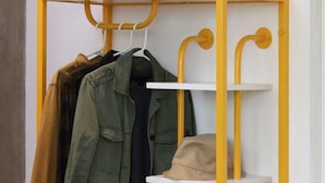 Een gele en witte opslagunit met planken om kleding op te hangen en een lager gelegen plank voor opslag.