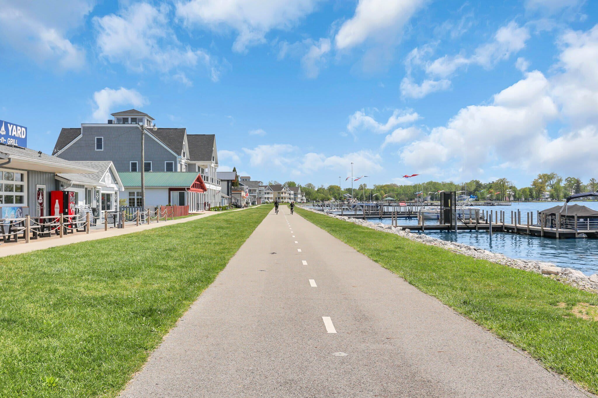 Een pad dat leidt naar een waterkant, met gebouwen aan de ene kant en een steiger aan de andere kant.