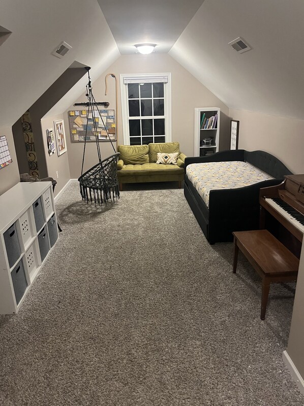 Une chambre mansardée chaleureuse avec un lit en mezzanine, un canapé vert, un petit bureau et un piano.