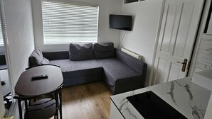A compact living space with a sofa, a small table, and a TV mounted on the wall. - Nice and Cosy one bed flat
 (Carshalton)