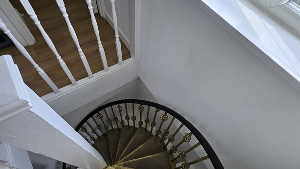 A spiral staircase with a wooden floor and white railings, leading to an upper floor. - Nice and Cosy one bed flat
 (Carshalton)