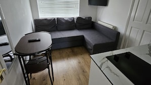 A compact living space with a sofa, a small table, and a TV mounted on the wall. - Nice and Cosy one bed flat
 (Carshalton)