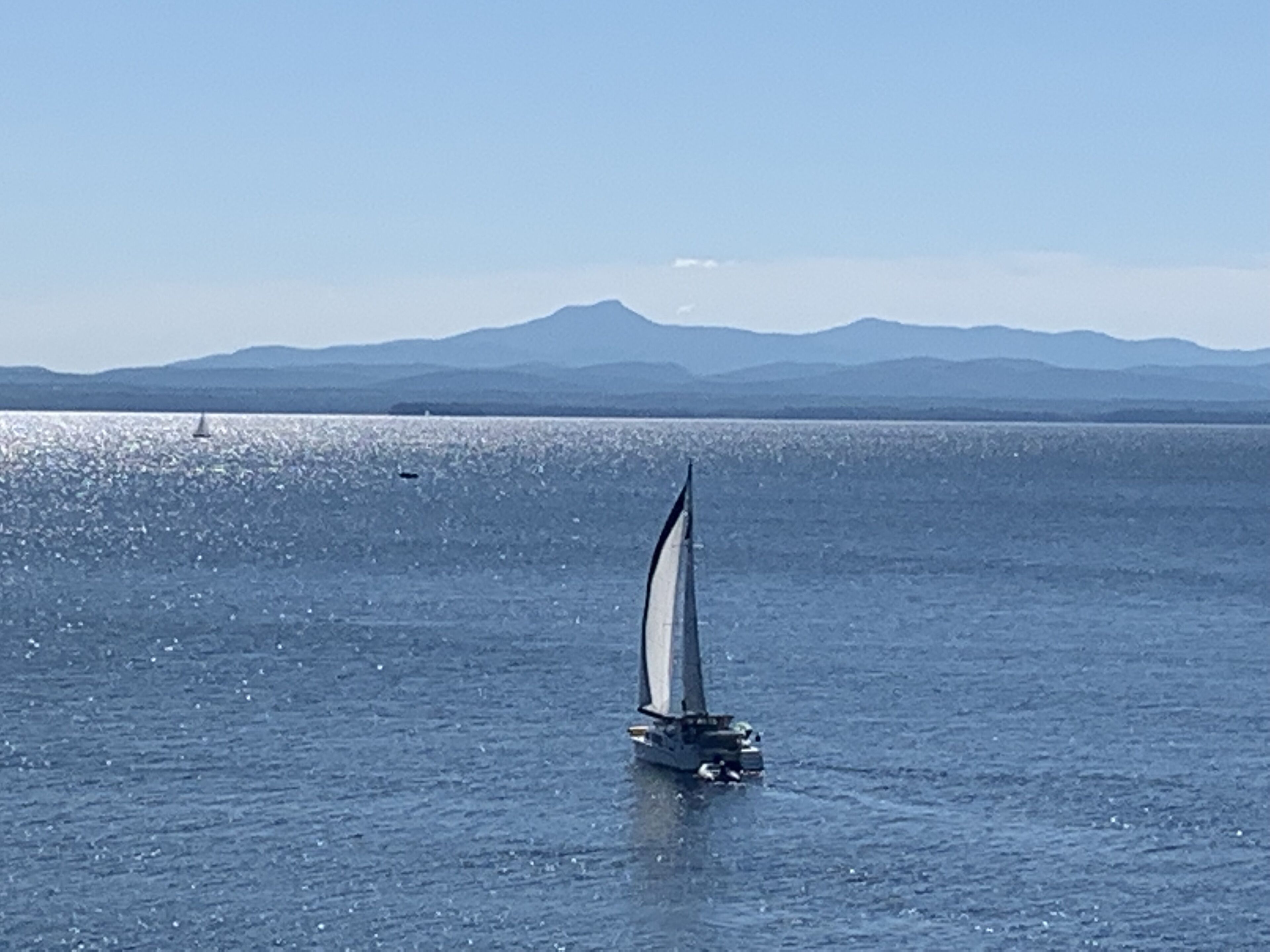 Een zeilboot op een kalm wateroppervlak met een bergketen op de achtergrond.