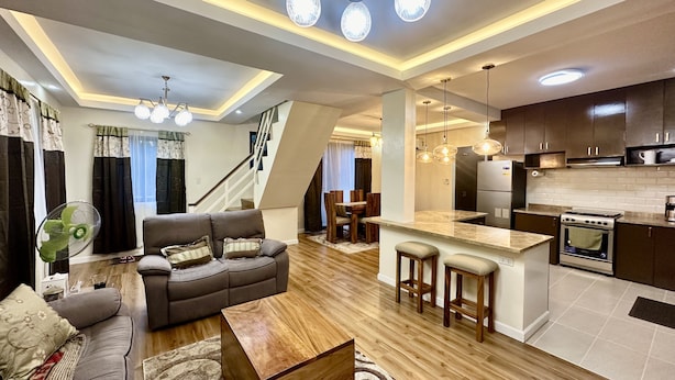 Una sala de estar moderna con sofá, mesa de centro y una cocina con estufa y taburetes de bar.